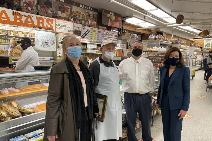 Manhattan BP Brewer, Len Berk, David Zabar, and LG Kathy Hochul stand, wearing masks, in front of Zabar's famed smoked fish counter